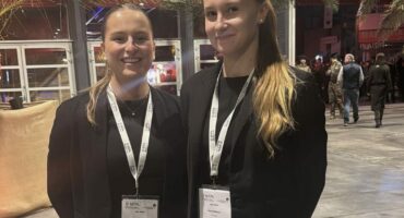 Deux hôtesses d'accueil professionnelles en tenue noire, souriantes, portant des badges et lanières personnalisées lors d'un événement d’entreprise.