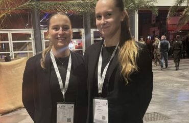Deux hôtesses d'accueil professionnelles en tenue noire, souriantes, portant des badges et lanières personnalisées lors d'un événement d’entreprise.
