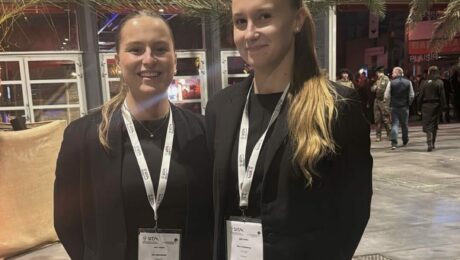 Deux hôtesses d'accueil professionnelles en tenue noire, souriantes, portant des badges et lanières personnalisées lors d'un événement d’entreprise.
